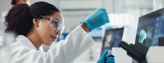 Female researcher in a laboratory using a pipette while analyzing scientific data displayed on a computer screen