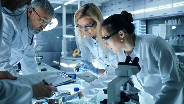 researchers in the lab looking at samples under microscope and holding clipboard