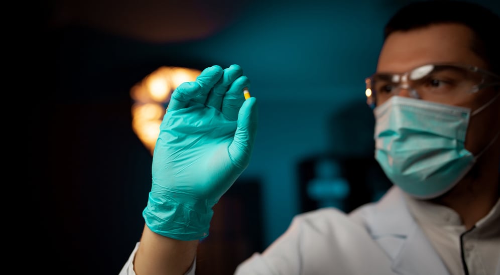 Lab scientist with lab gloves and mouth mask holding a yellow pill