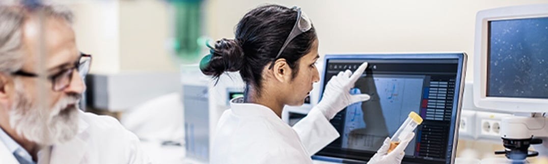 female scientist in the lab looking at the label of a test tube and touching her computer screen