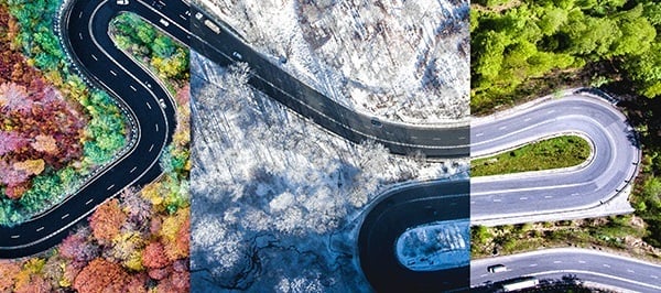 a winding road divided into three sections, each representing a different season. On the left, vibrant autumn foliage surrounds the road; in the center, a snowy winter landscape dominates; and on the right, lush green trees signal spring or summer.