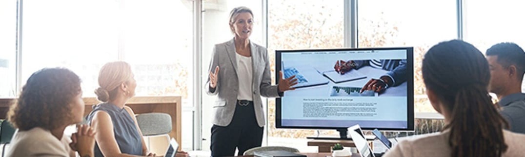 Women presenting next to a screen to her co-workers