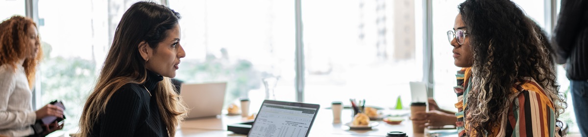 People working together at a table with laptops, coffee cups, and pastries in a bright office setting